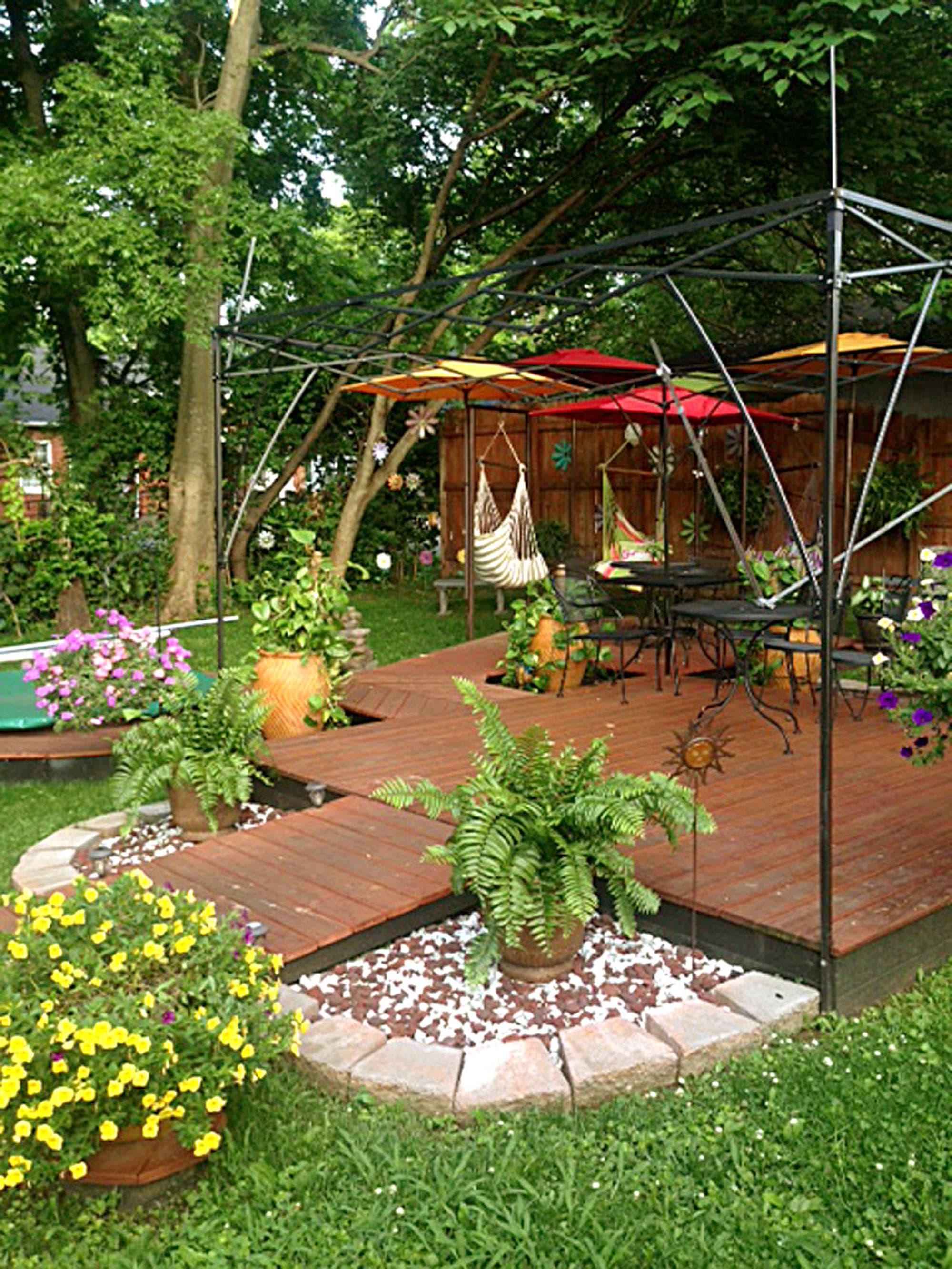 The InSPAration Garden: a wood deck with hanging chairs, umbrellas, ferns and flowers under mature trees